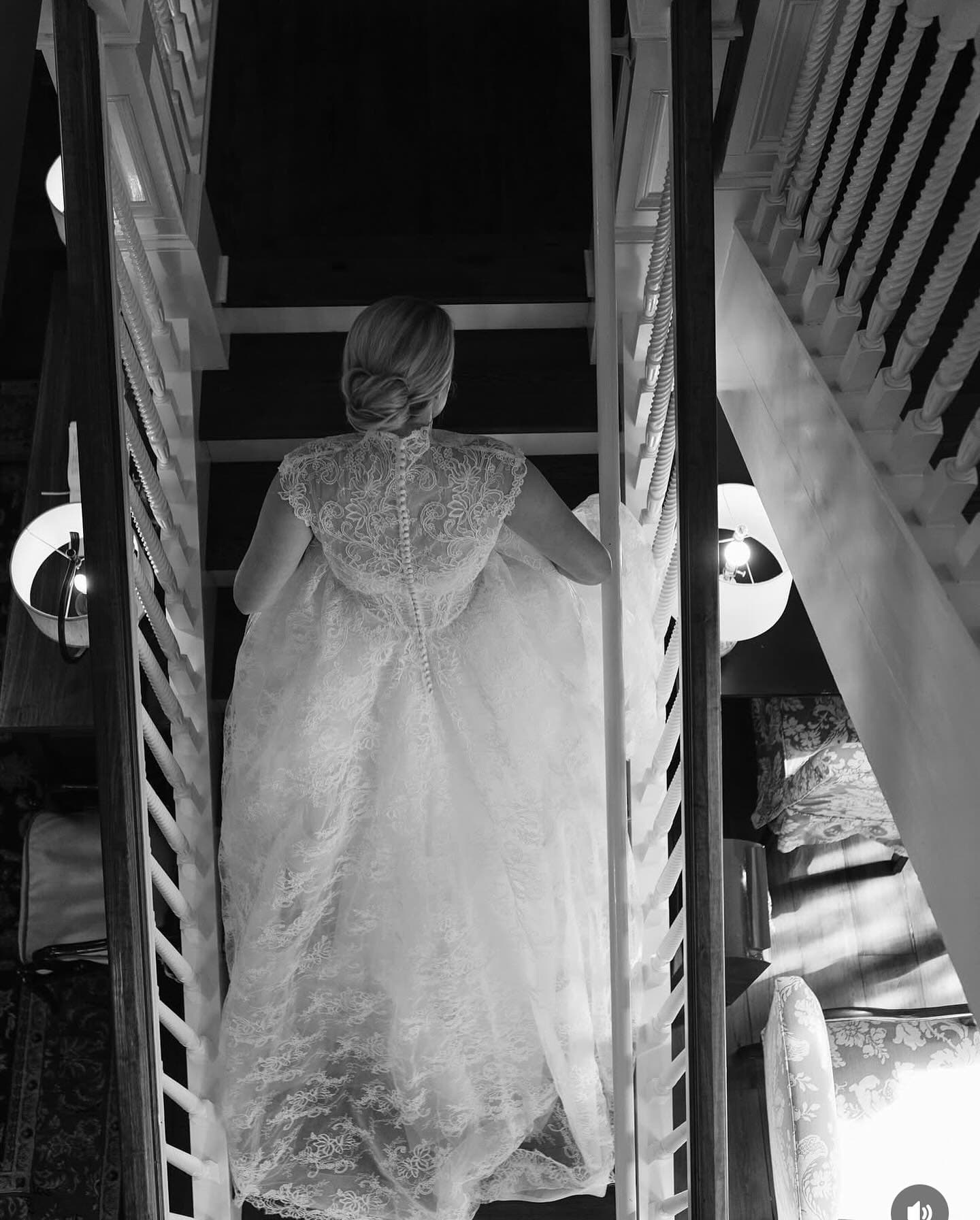Bride with a low bun in a lace gown on a staircase, black and white