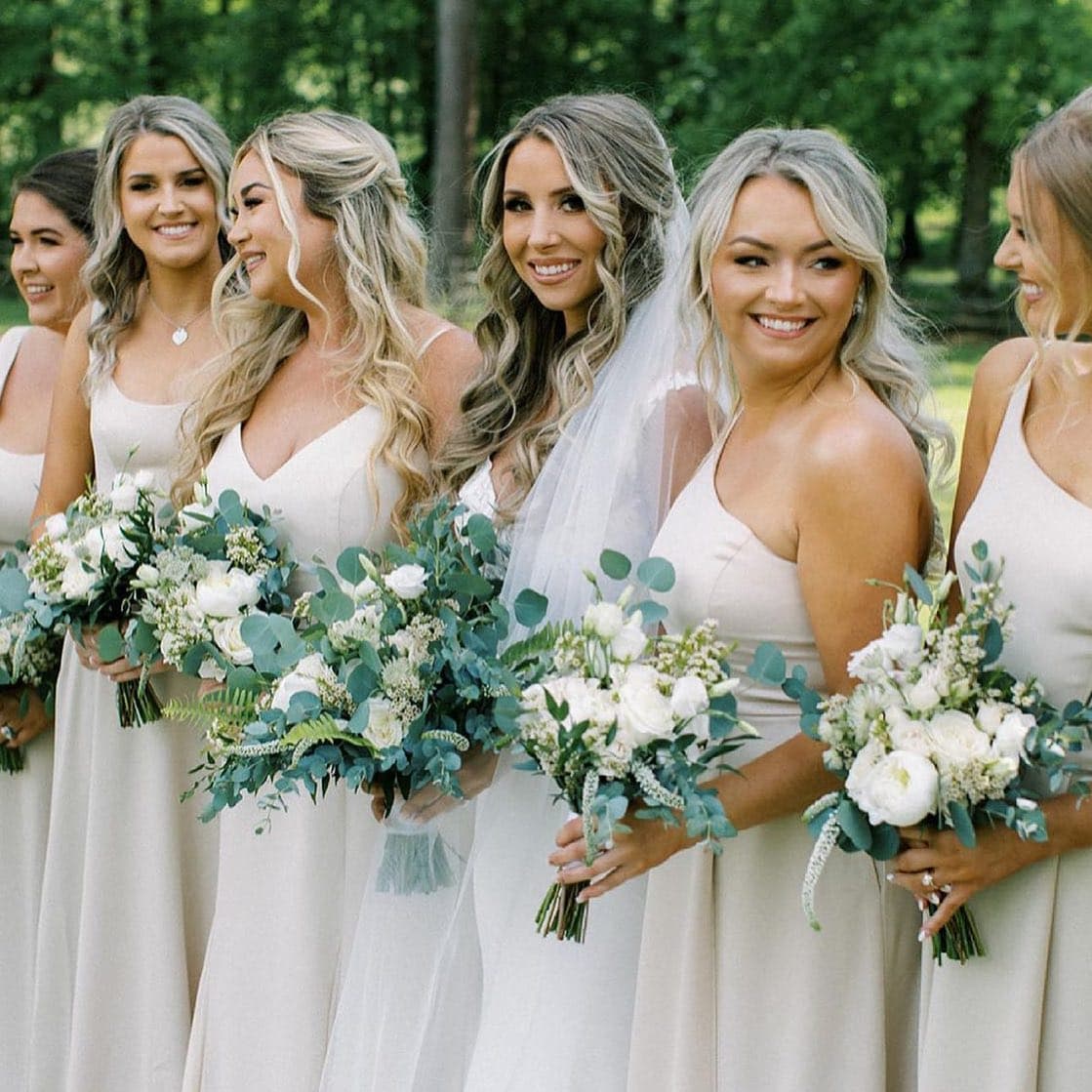 Bridesmaids with soft curls holding greenery and white bouquets